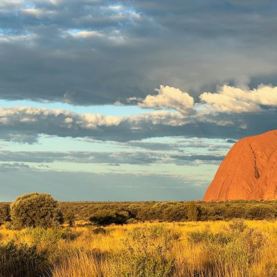A breathtaking sunset view of the iconic Uluru rock formation surrounded by the Australian outback landscape.