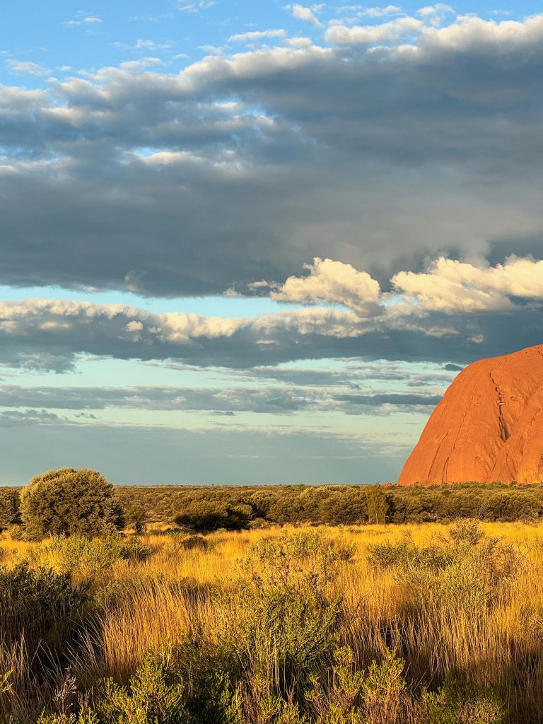 A breathtaking sunset view of the iconic Uluru rock formation surrounded by the Australian outback landscape.