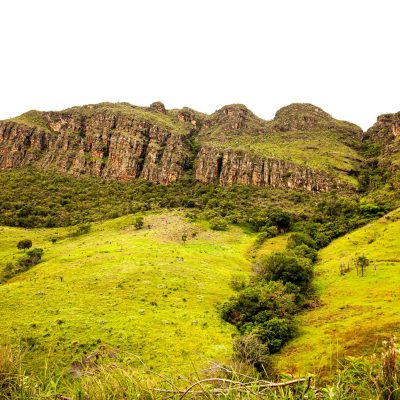 Scenic view of lush green hills and rocky formations on a sunny day.