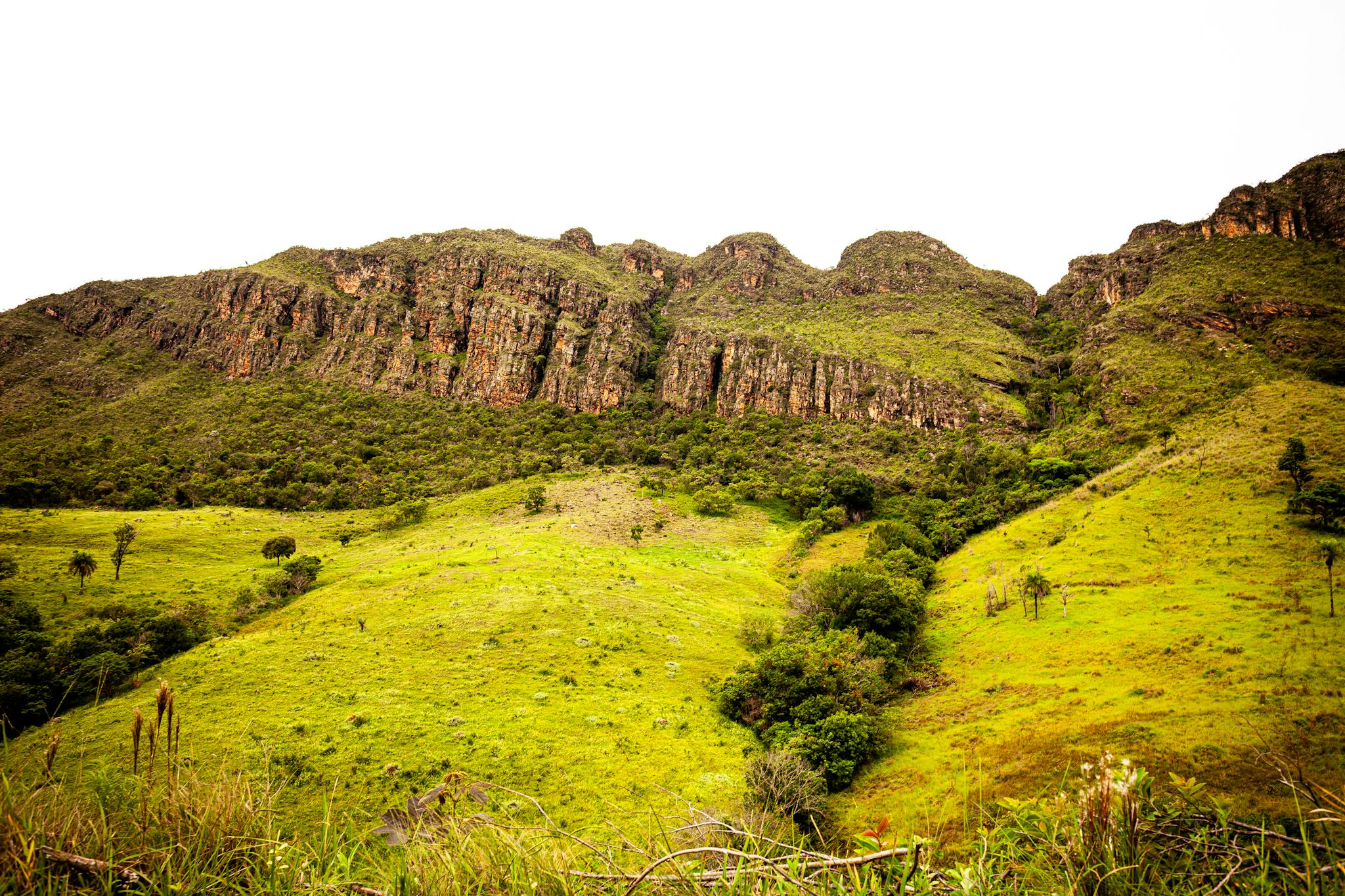 Scenic view of lush green hills and rocky formations on a sunny day.