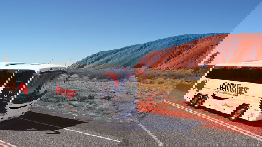 An AAT Kings tourist coach driving on the sealed Lasseter Highway toward the Red Centre